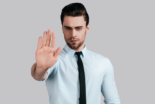 Serious young man in white shirt and tie gesturing and looking at camera while standing against grey background photo