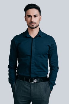 Confident in his style. Handsome young man hands keeping in pockets and looking at camera while standing against grey background photo