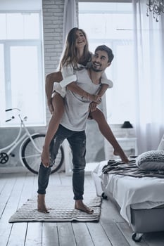 Playful couple. Handsome man in white T-shirt carrying young attractive woman on shoulders while spending free time at home photo