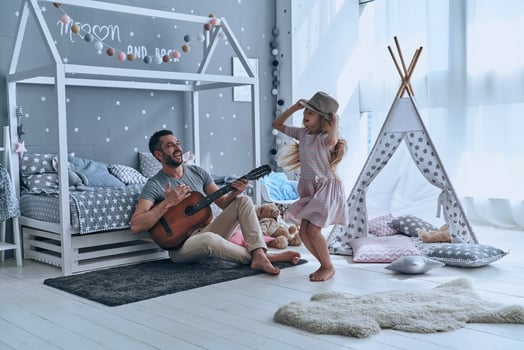 Having fun together. Young father playing guitar for his little daughter and smiling while spending free time at home photo