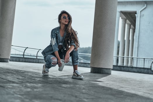 She is all about fashion. Beautiful young woman in jeans wear looking away and holding a disposable cup while spending time outdoors photo