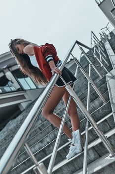 In sport style. Full length of beautiful young woman in sports uniform leaning on the railing while posing on the stairs outdoors photo