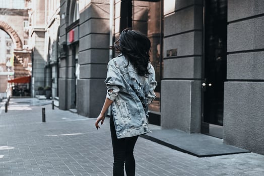 City style. Rear view of young woman in denim jacket walking down the street photo