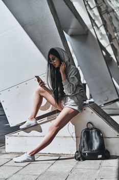 Let the music take you away. Beautiful young woman in casual wear holding a smart phone while sitting outdoors photo