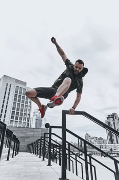 Jumping straight over any obstacles. Full length of handsome young man in sport clothing jumping over railing while exercising outside photo