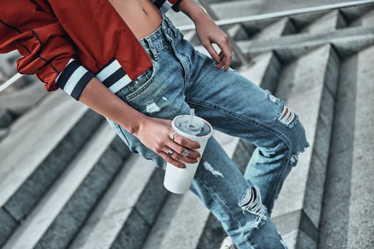 Enjoying cold drink. Close-up of young woman in casual wear holding a disposable cup while walking down the stairs outdoors photo