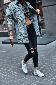 Perfect style. Close-up of young woman adjusting her denim jacket while walking down the street photo