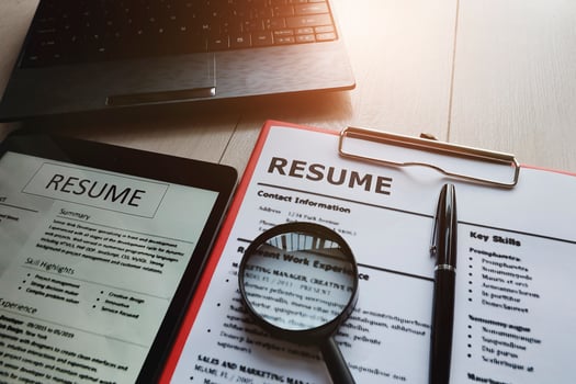 Close-up of resume with magnifying glass, computer laptop and pen on wooden background photo
