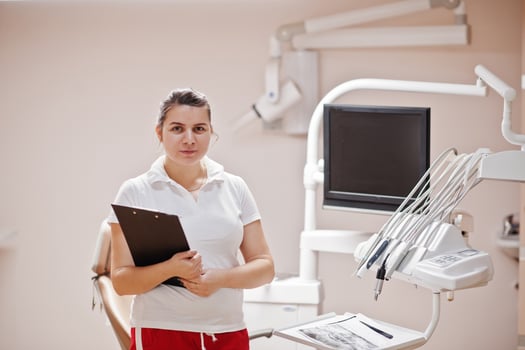 Portrait of female dentist woman standing in her dentistry office with clipboard on hands. photo