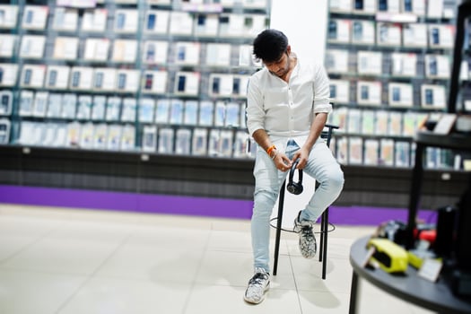 Indian man customer buyer at mobile phone store with wireless earphones sitting on chair. South asian peoples and technologies concept. Cellphone shop. photo