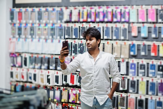 Indian man customer buyer at mobile phone store making selfie on his new smartphone with case. South asian peoples and technologies concept. Cellphone shop. photo