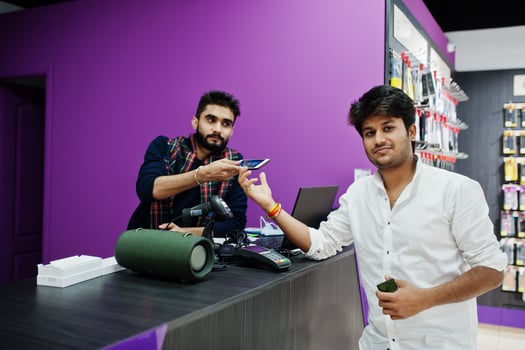 Indian man customer buyer pay for his new smartphone for seller by credit card at mobile phone store. South asian peoples and technologies concept. Cellphone shop. photo
