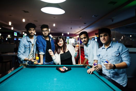 Group of stylish asian friends wear on jeans playing pool billiard on bar. photo