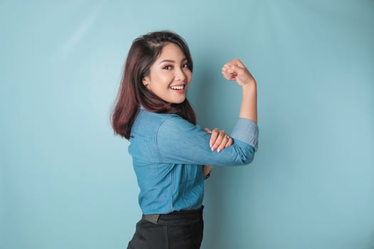 Excited Asian woman wearing a blue shirt showing strong gesture by lifting her arms and muscles smiling proudly photo