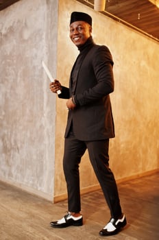 Strong powerful african american man in black suit and turtleneck and cap, with elephant tusk. photo