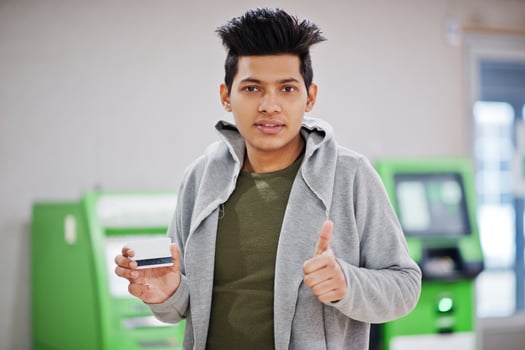 Young stylish asian man with credit card in hand show thumb up against row of green ATM. photo