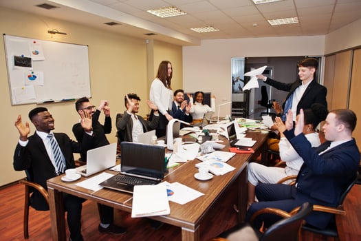 Multiracial business team meeting around boardroom table, two team leaders throw paper up. photo