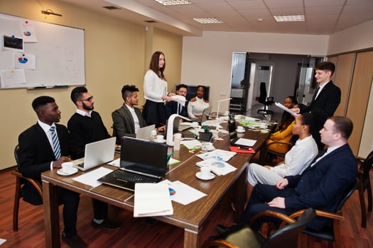 Multiracial business team meeting around boardroom table, two team leaders throw paper up. photo