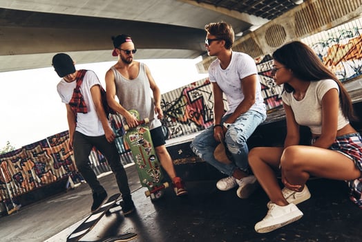 Taking a break. Group of young modern people talking while spending time at the skateboard park outdoors photo