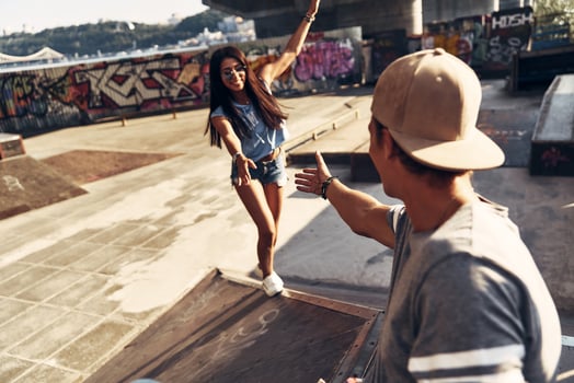 Beautiful young woman trying to climb up to her friend while spending time at the skate park outdoors photo