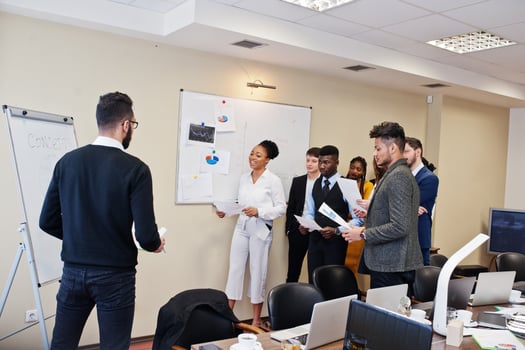 Mixed race business coach presenting report standing near whiteboard pointing on sales statistic shown on diagram and chart teach diverse company members gathered together in conference room. photo