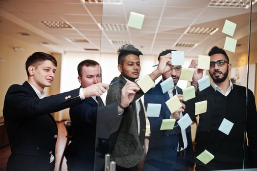 Business mans pointing on glass with colorful paper notes. Diverse group of male employees in formal wear using stickers. photo