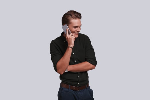 Handsome young man talking on smart phone and smiling while standing against grey background photo
