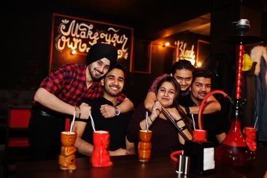Group of indian friends having fun and rest at night club, drinking cocktails and smoke hookah. photo