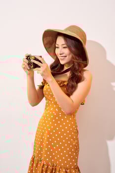 Attractive young woman with a photo camera in her hand on an isolated beige background. The concept travel