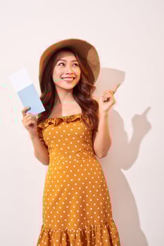 A young woman in a orange polka dots dress with a straw hat on her head is holding a passport and plane tickets photo