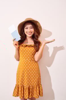A young woman in a orange polka dots dress with a straw hat on her head is holding a passport and plane tickets photo