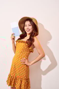 A young woman in a orange polka dots dress with a straw hat on her head is holding a passport and plane tickets photo