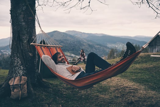 Nice evening. Handsome young man lying in hammock and smiling while camping with his girlfriend photo