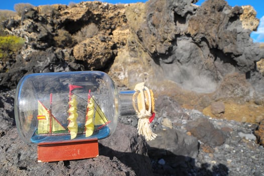 a bottle with a sailboat in it on a rock photo