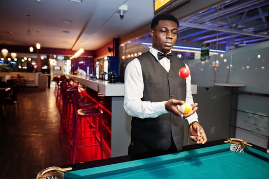 Young handsome african man wearing white shirt, black vest and bow tie play pool billiard. photo