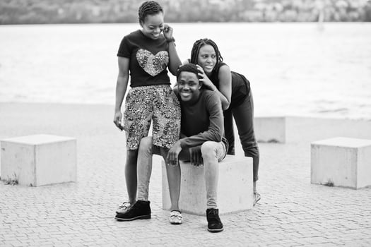 Three african american friends sitting on stone cubes outdoor. photo