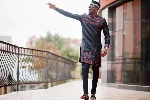 Handsome afro american man wearing traditional clothes, cap and eyeglasses in modern city raised his hand. photo