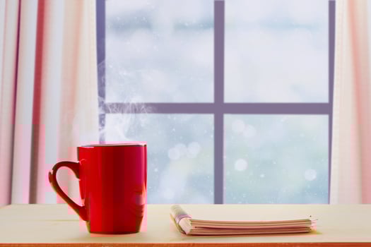 A Red mug Hot coffee and notebook at Beside the windows at winter and falling snow photo