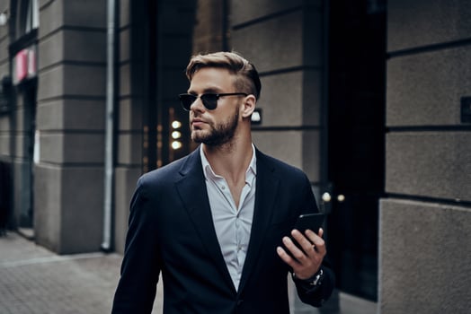 Confidence and style. Handsome young man in smart casual wear holding his smart phone while standing outdoors photo
