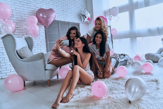 Show smile Four attractive young women in pajamas smiling while taking selfie in the bedroom with balloons all over the place photo