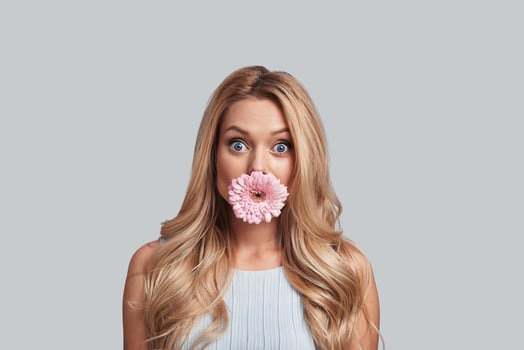 Beautiful like flower. Attractive young woman with flower covering mouth staring at camera while standing against grey background photo