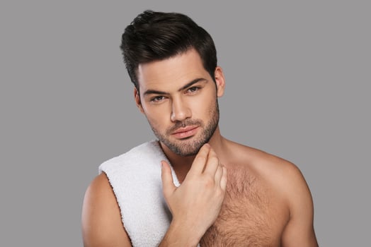 He is looking right into your heart. Handsome young man looking at camera and keeping hand on chin while standing against grey background photo