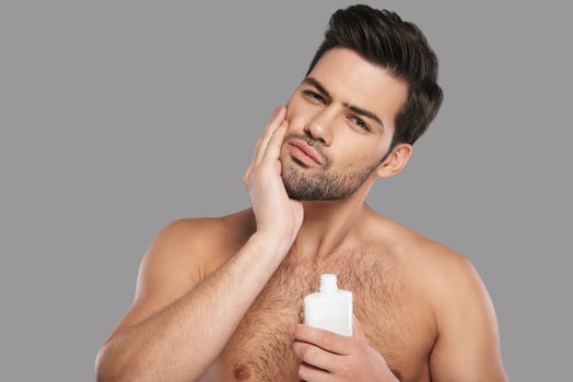 Used to look perfect. Handsome young man applying aftershave lotion and smiling while standing against grey background photo