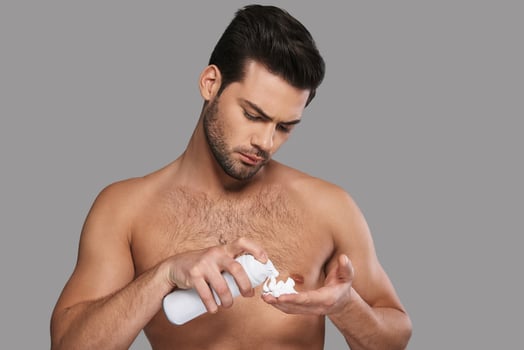 Got to shave. Handsome young man applying shaving cream while standing against grey background photo