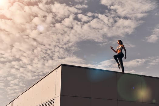 Power and beauty. Full length of modern young woman in sports clothing jumping while exercising time on the roof outdoors photo