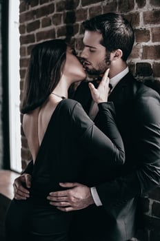 Tender kiss. Beautiful young loving couple bonding to each other and kissing while both standing against brick wall indoors photo