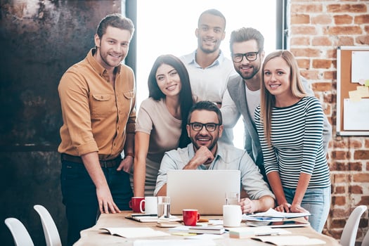 Perfect creative team. Group of six cheerful young people looking at camera with smile while leaning to the table in office photo