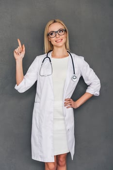 Recommendation from your doctor. Beautiful young female doctor pointing on copy space and looking away with smile while standing against grey background photo