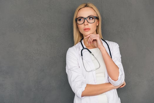 Interesting medical case. Beautiful young female doctor looking thoughtful and keeping hand on chin while standing against grey background photo