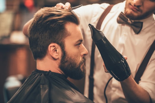 Looking good already. Close up side view of young bearded man getting groomed by hairdresser with hair dryer at barbershop photo